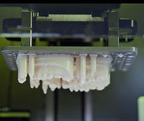 A resin 3D printer actively building multiple dental models or surgical guides on a build platform, showcasing the additive manufacturing process.