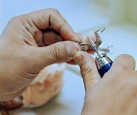 Close-up of an expert technician's hands skillfully refining a dental prosthetic on a physical model, demonstrating the commitment to manual quality control and perfect fit.