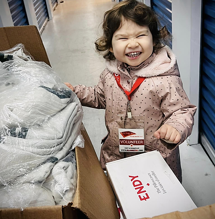 Young girl wearing pink jacket and red lanyard helps sort blankets while smiling at the camera.