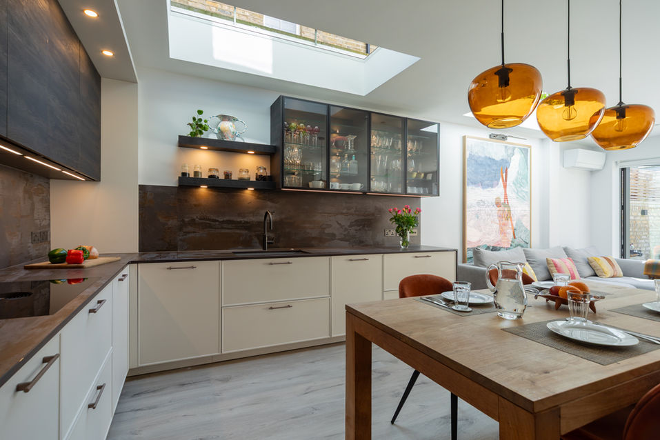 Open-plan kitchen with dining table, glass cabinetry and natural light from roof glazing