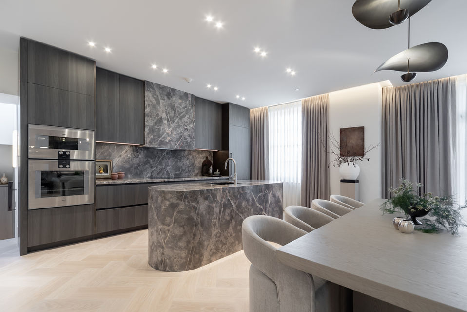 Wide view of contemporary kitchen and dining area with marble waterfall island, dark cabinetry and recessed lighting