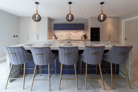 Wide view of modern kitchen with marble island, upholstered bar stools and pendant lighting.