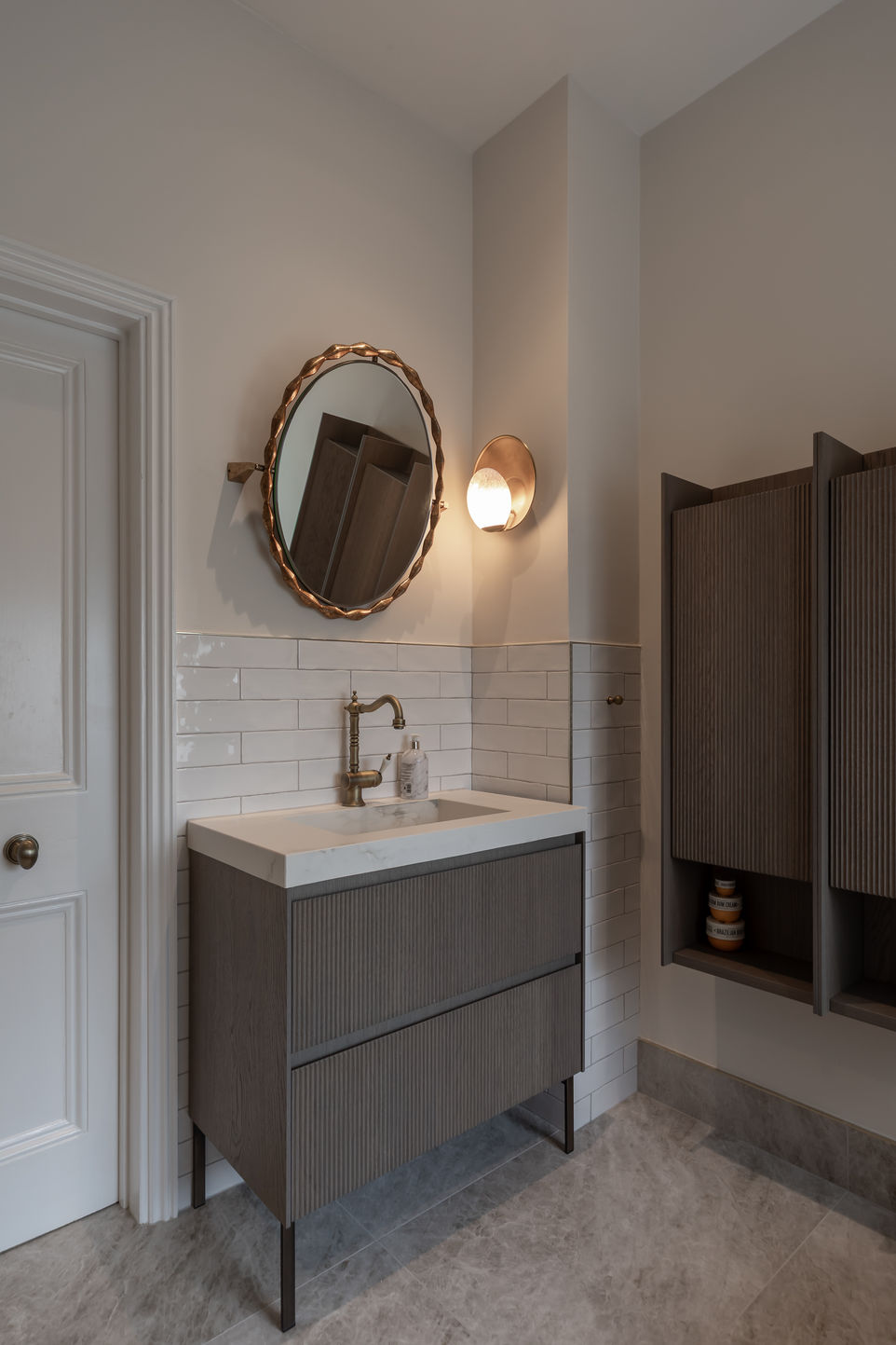 Vertical image of the floating vanity with round mirror and wall sconce in a modern Fulham bathroom.