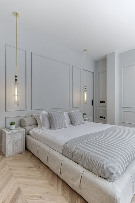 Calm bedroom with upholstered bed, panelled wall and pendant bedside lighting.