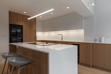 Contemporary kitchen with white waterfall island and warm timber cabinetry, photographed in London.