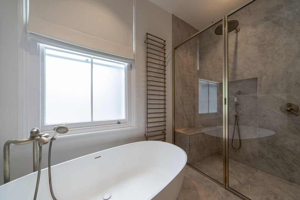 Freestanding bath next to glass shower enclosure with natural light from a large window.