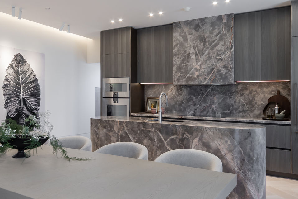 View from dining area into modern kitchen with dark cabinetry, marble splashback and feature island.