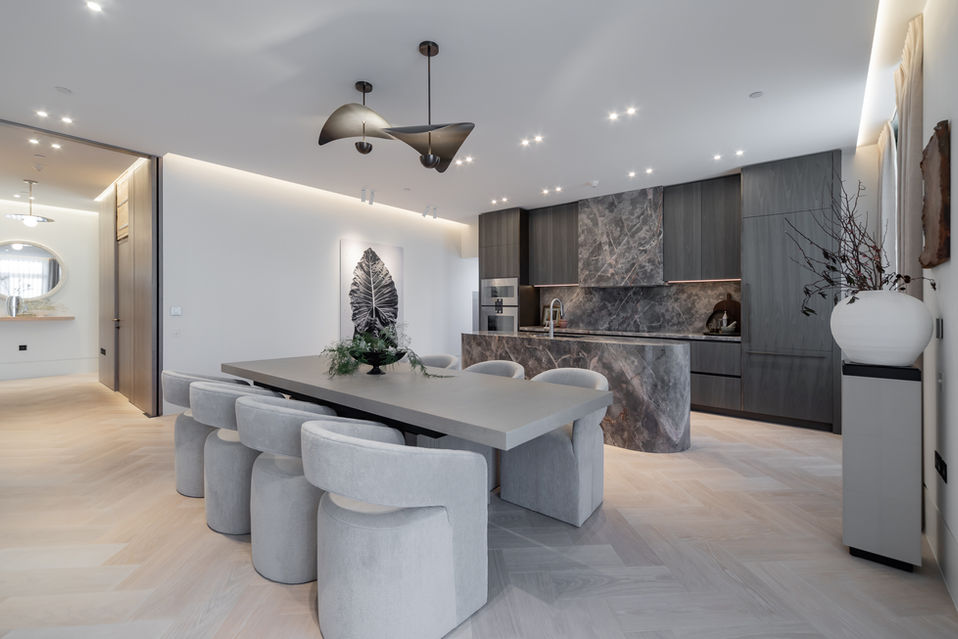 Open-plan kitchen with a long dining table, a sculptural island, and modern lighting in a bright interior.