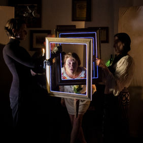 An actor looking through several picture frames held up by 2 other actors