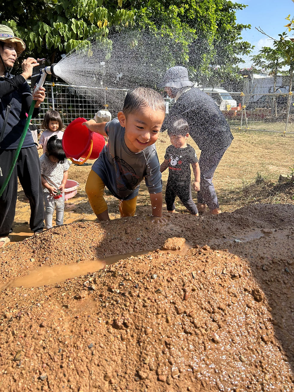 泥遊びをする子供たちが、バケツとホースを使って、喜名こども園で遊んでいます。