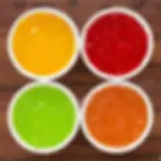 Four bowls of colorful jello—yellow, red, green, and orange—are arranged on a wooden surface, creating a vibrant and appetizing display.