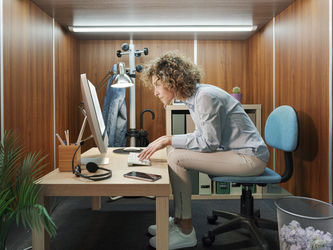 Woman sitting a small desk hunched over looking at a screen