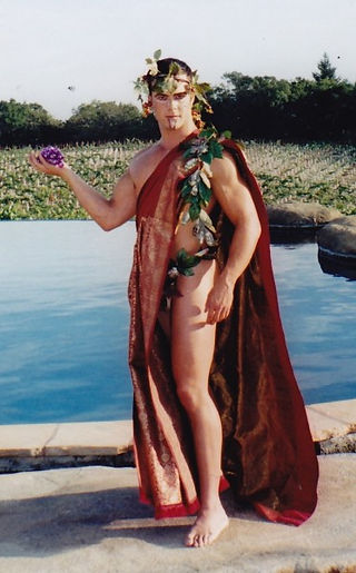 Man dressed in a toga with a grapevine crown, by a pool, holding grapes. Background shows greenery and water, creating a serene vibe.