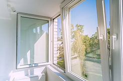 An open white plastic window in a bright, minimalist apartment balcony, letting in sunligh
