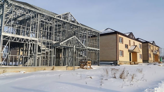 Two buildings, one under construction, in snowy landscape.