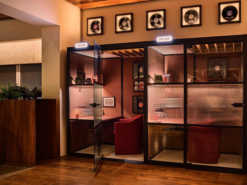 Recording studio with "On Air" signs, vinyl records on the wall, and red chairs. Warm lighting creates a cozy atmosphere.