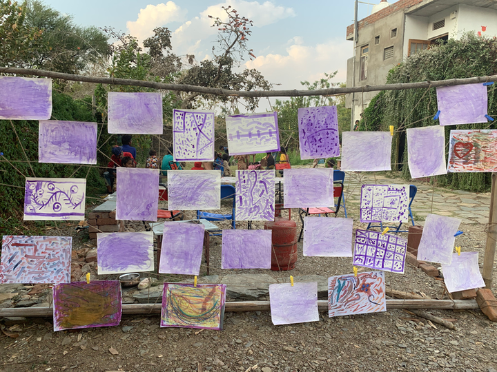 A wooden frame with a grid, consisting various rectangles of paper consisting paintings by children using violet coloured ink