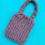Thumbnail: Purple hand-knitted purse with short handle made with thick soft yarn on aqua chair