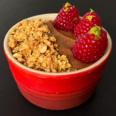 an orange ramekin filled with chocolate mouse topped with an oaty cruble and three fresh raspberries and some grated lime zest