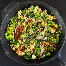A cast-iron black skillet on a stove-top with a hash of turkey mince, broccoli and red onions