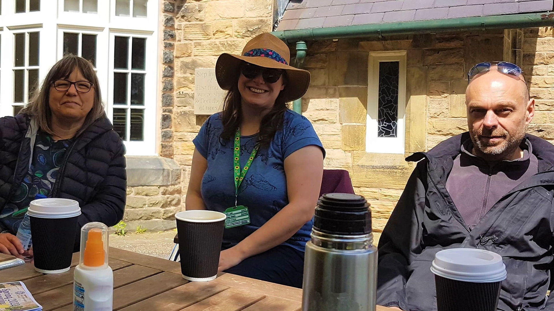 Three attendees at the Picnic, with hot drinks in front of them.