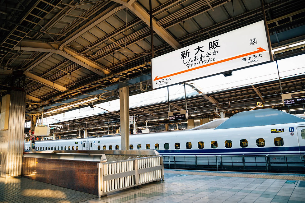 Shinkansen train at Shin-Osaka station platform, with overhead sign in Japanese and English. Empty with bright sunlight filtering in.