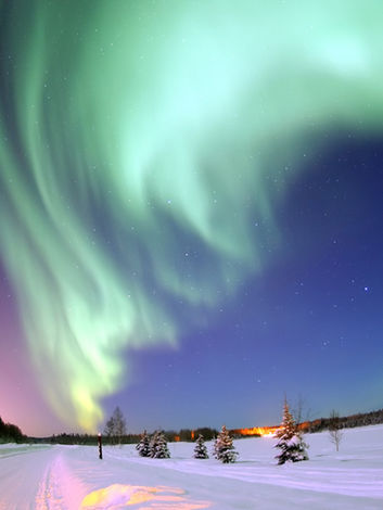 Northern Lights dancing above snow-covered landscape in Alaska at night.