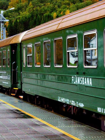 Green Flåm Railway train standing at mountain station in Norway.