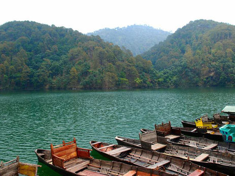 A serene lake in Sattal surrounded by forested hills, with wooden boats resting along the shore, reflecting the tranquil landscape of Kumaon’s birding region.
