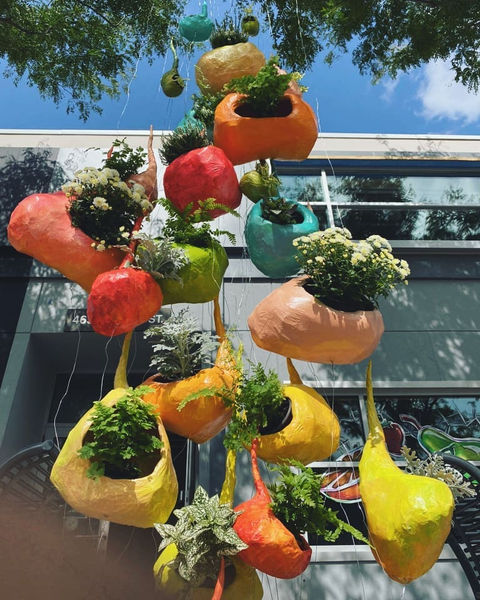 Recycled eco-art installation titled Nesting by Canadian artist Emma Lee Fleury, featuring suspended, colorful hive-like forms filled with living plants, created from reclaimed materials and installed outdoors during Niagara Falls Night of Art 2020, exploring themes of habitat, community, pollinators, and environmental awareness.