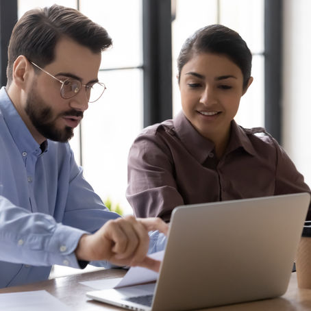 Two colleagues collaborate at a desk, reviewing brand guidelines on a laptop. They appear focused and engaged, discussing key elements such as logos, colors, and tone to ensure brand consistency for a small business.