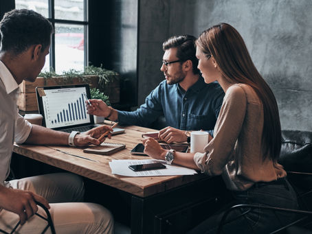 Two women collaborate at a desk while reviewing a small business marketing plan on a laptop. They are engaged in strategic planning, discussing goals and ideas for an effective DIY marketing strategy.