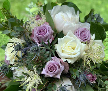a bridal bouquet of lavender and white roses blended with blue thistle and textural greens