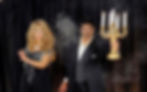 Shahid Malik and Lisa holding a lit Candelabra with smoke, against a black background.