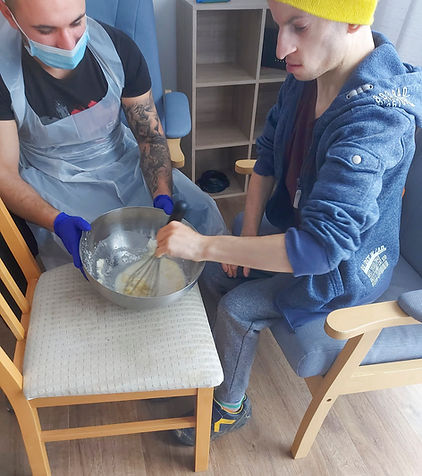 Male domicialiary care worker helping a young man to whisk an egg