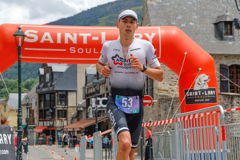 Triatleta corriendo bajo un arco de meta con el número 53 en su pecho.