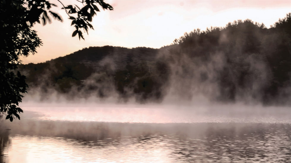 Misty lake scene at Rocky Gap Lake with fog rising from the water, forested hills in the background, soft light from sunrise or sunset, and tree branches framing the view—evoking natural stillness and early morning calm.