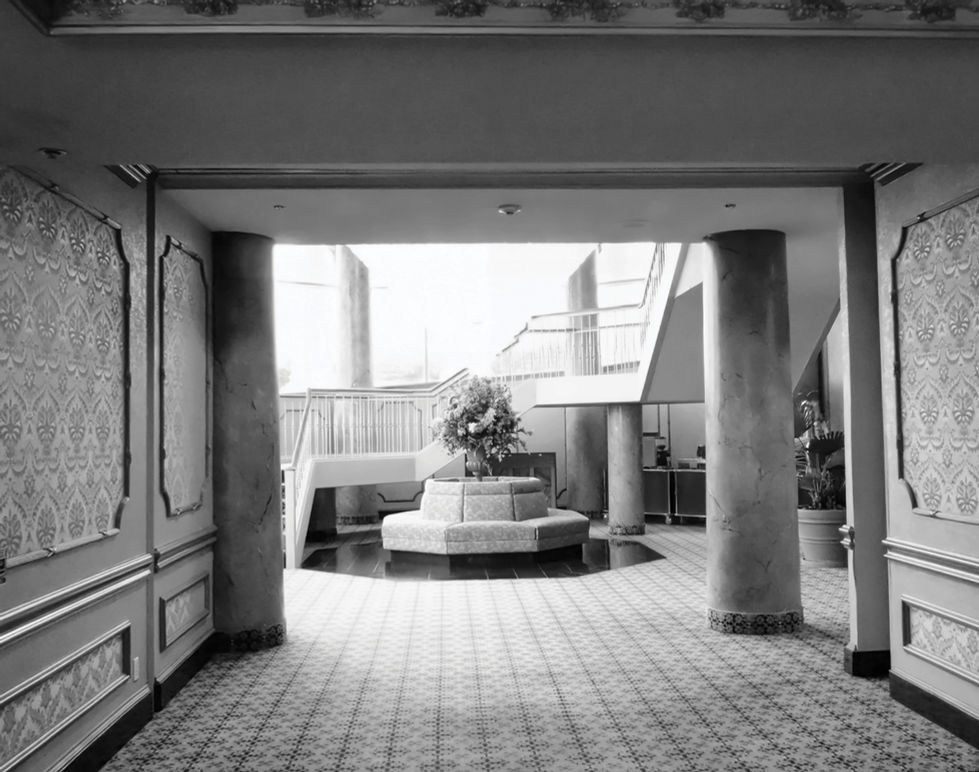 Interior space with a central circular planter or fountain, geometric tiled floor, large columns, decorative wall paneling, and stairs in the background; natural light from above highlights architectural symmetry and civic atmosphere.