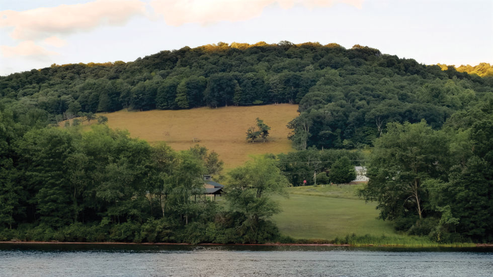 Scenic landscape at Flintstone Park with a brown field in the middle ground, green grassy foreground with scattered trees and small buildings, and forested hills in the background under a partly cloudy sky.