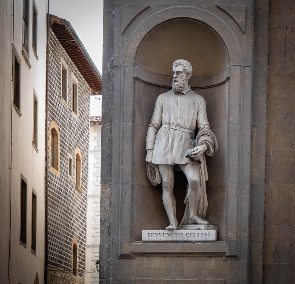 Statue of Giovanni delle Bande Nere standing in a niche, wearing historical attire and holding a scroll; nameplate below identifies him, with traditional European buildings in the background.