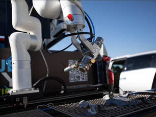 A spray painting robot poised over metal parts