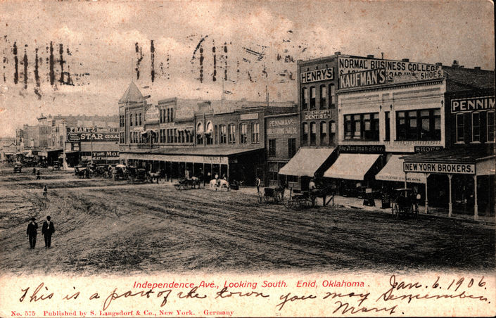 A vintage postcard with a black and white photograph of an unpaved street lined with buildings