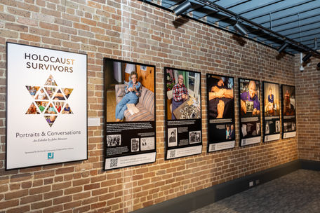 A series of wall-mounted posters, one reading "Holocaust Survivors: Portraits and Conversations," the others displaying portraits and small text.