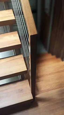Close-up architectural detail of bespoke residential staircase joinery featuring open-riser hardwood timber treads with contrasting dark stained timber stringer, tensioned stainless steel wire cable balustrade with precision-fitted vertical dark steel post, and warm-toned engineered hardwood flooring — custom staircase joinery and construction by Premier Form Pty Ltd, Melbourne Victoria Australia