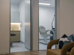 Compliant medical clinic fitout featuring modern consultation rooms, seamless vinyl flooring, custom timber laminate vanity cabinetry with brass fixtures, and an adjustable patient treatment chair.