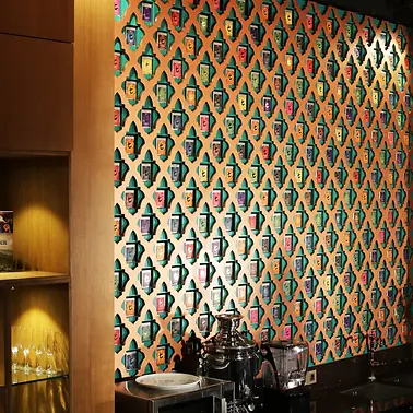 Bespoke hospitality and retail interior featuring a full-height custom timber geometric lattice feature wall displaying multicoloured specialty tea product tins in individual alcoves, warm oak timber open shelving unit with integrated downlighting displaying glassware and tea canisters, exposed brick wall, dark granite benchtop with chrome tea urn and service equipment, and warm ambient recessed lighting — custom retail joinery and hospitality fitout by Premier Form Pty Ltd, Melbourne Victoria Australia