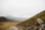 Hikers in the distance walking along trail in rolling green hills under gray cloudy and foggy skies 