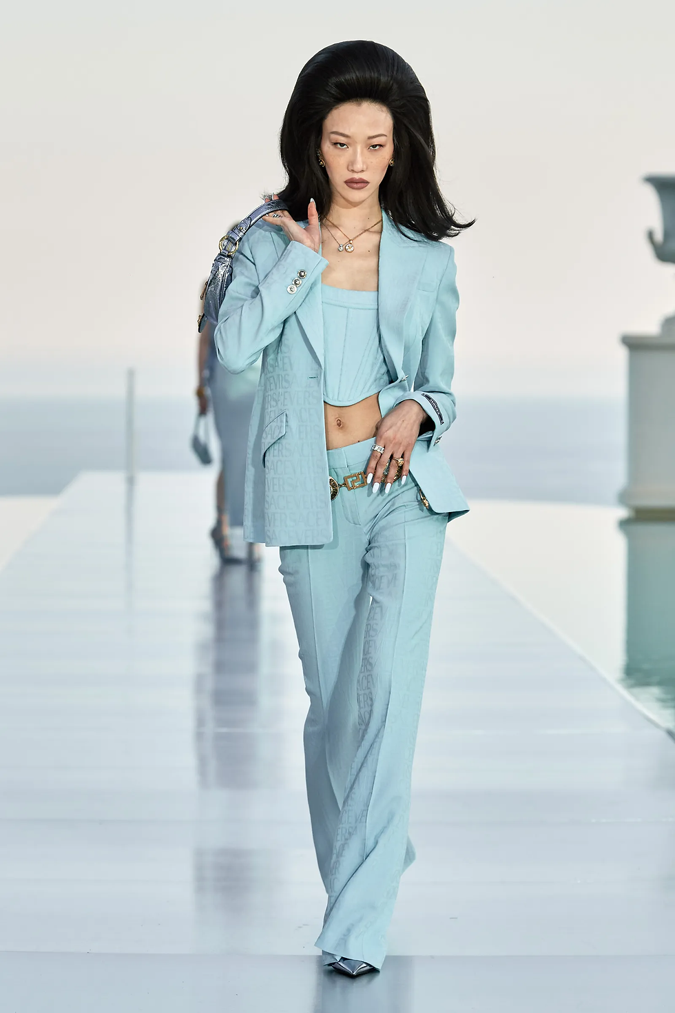 Pale blue Dua Lipa x Versace corset with matching trouser suit, gold chain belt , blue metallic leather handbag and blue heels.