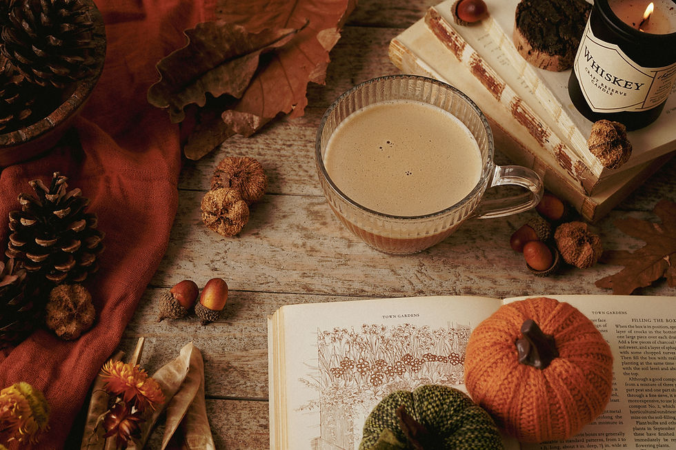Nature morte d’automne chaleureuse: tasse crémeuse, livre ouvert, citrouilles tricotées, bougie Whiskey allumée sur bois.