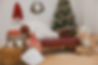 Coast Santa Studio Christmas scene including red leather chaise surrounded by rustic Christmas themed details including a large Christmas tree, presents, Santa's sack and coat.